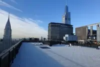 Snow-covered rooftop with NYC skyline and modern skyscrapers on a clear day.