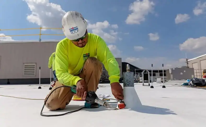 Commercial roofing worker installing TPO membrane under blue sky.