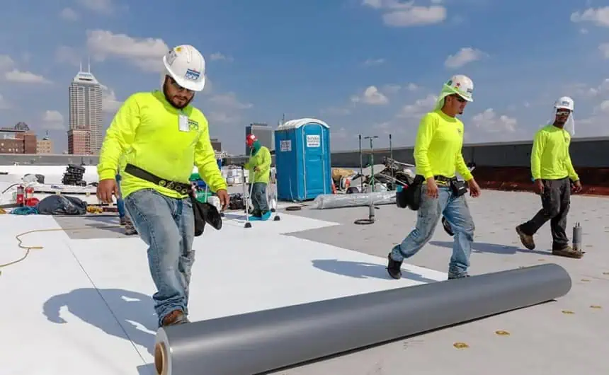 Construction workers installing TPO roofing membrane on manufacturing plant rooftop.