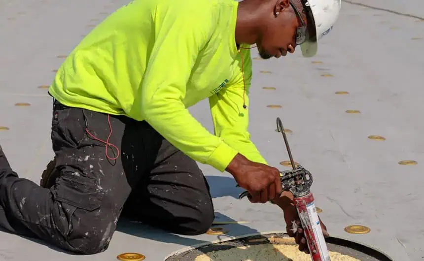 Worker in neon green shirt applying sealant with caulking gun