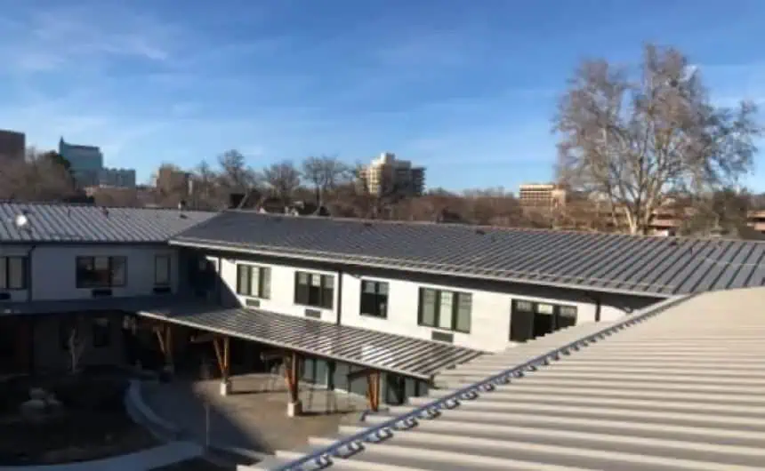 Modern metal roofs in courtyard with clear blue sky, mid-rise buildings, and bare trees.