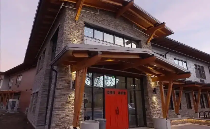 Modern building with stone walls, wooden beams, and red double door entrance.