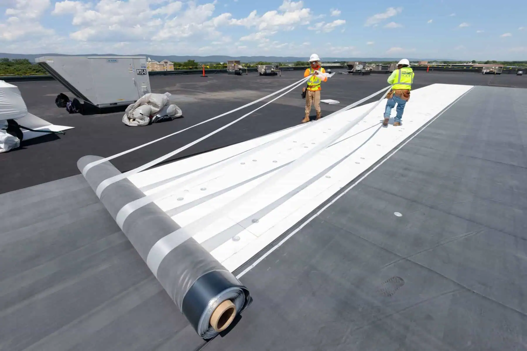 Workers installing single ply membrane on commercial flat roof under blue sky