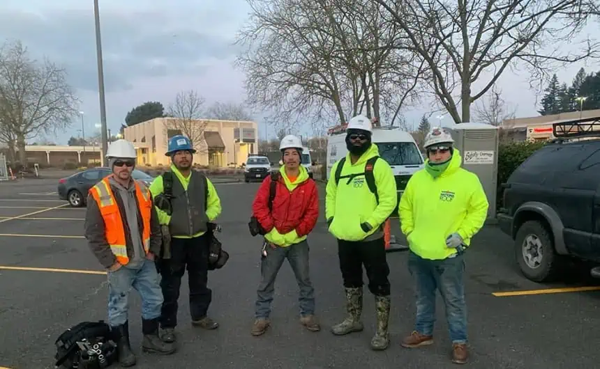 Five workers in safety gear, parking lot; Portland's cityscape with gastropubs in the background.