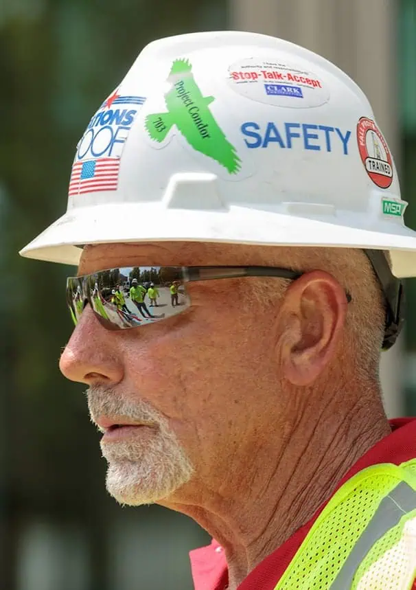 Older worker in safety gear overlooks TPO roofing team