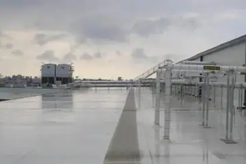 Wet industrial flat roof with metal piping, conduits, and nearby cold storage facility.