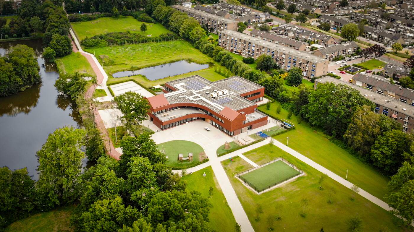 Aerial view of school roofing amidst green courtyard and pond.