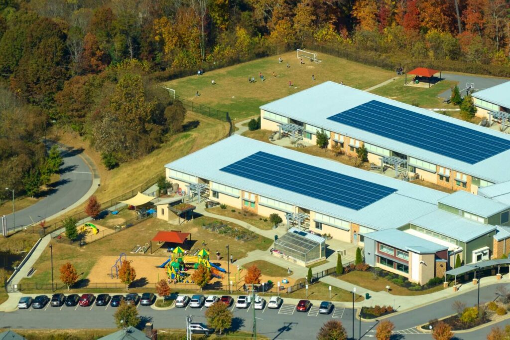 Aerial view of modern school with solar panels, playground, and sports field. Sustainable campus amid fall foliage.