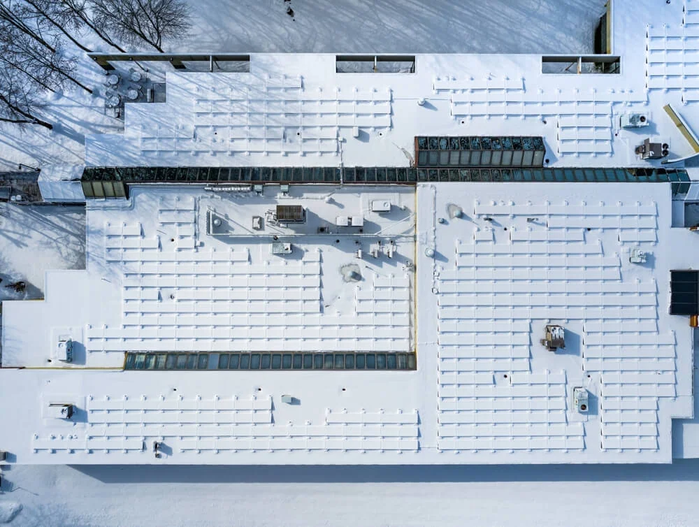 Commercial building with flat roof and dozens of solar panels covered in snow.