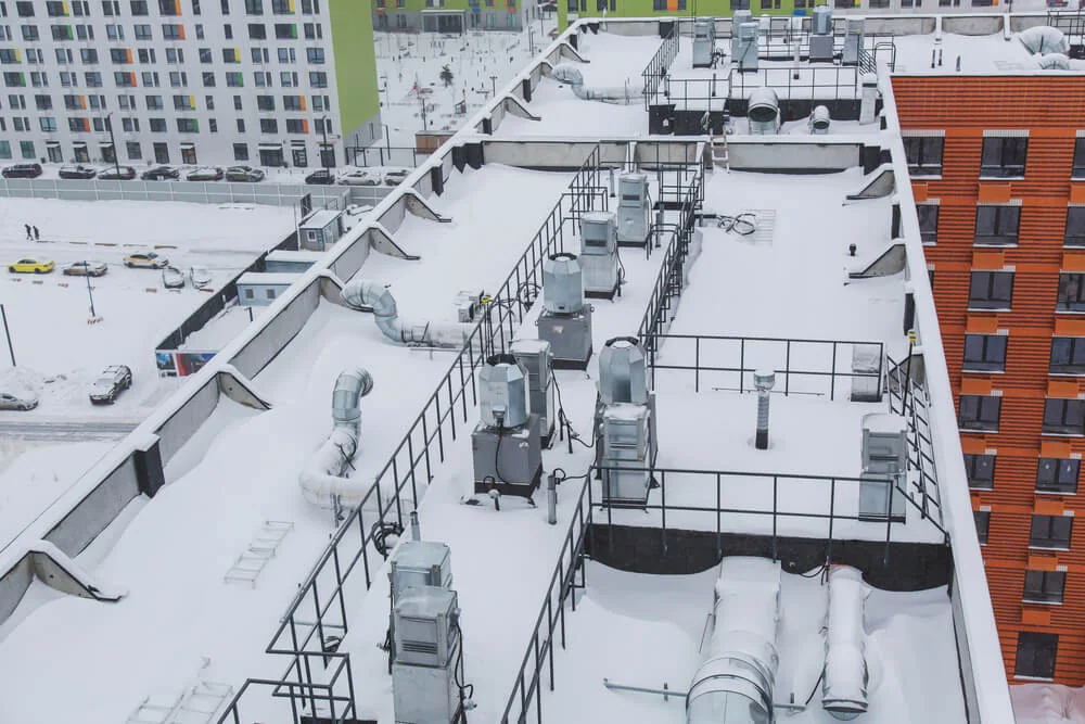 Snow-covered commercial flat roof with railings and mechanical equipment.