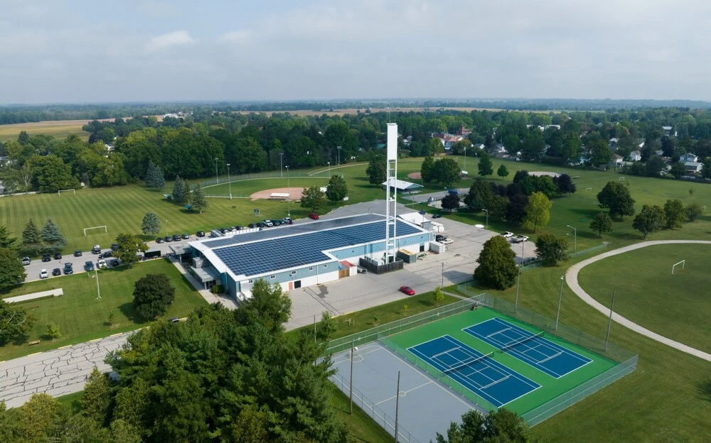 Aerial view of a sports facility showcasing commercial roofing with solar panels, including EPDM and TPO roofs, adjacent tennis courts, and open fields.