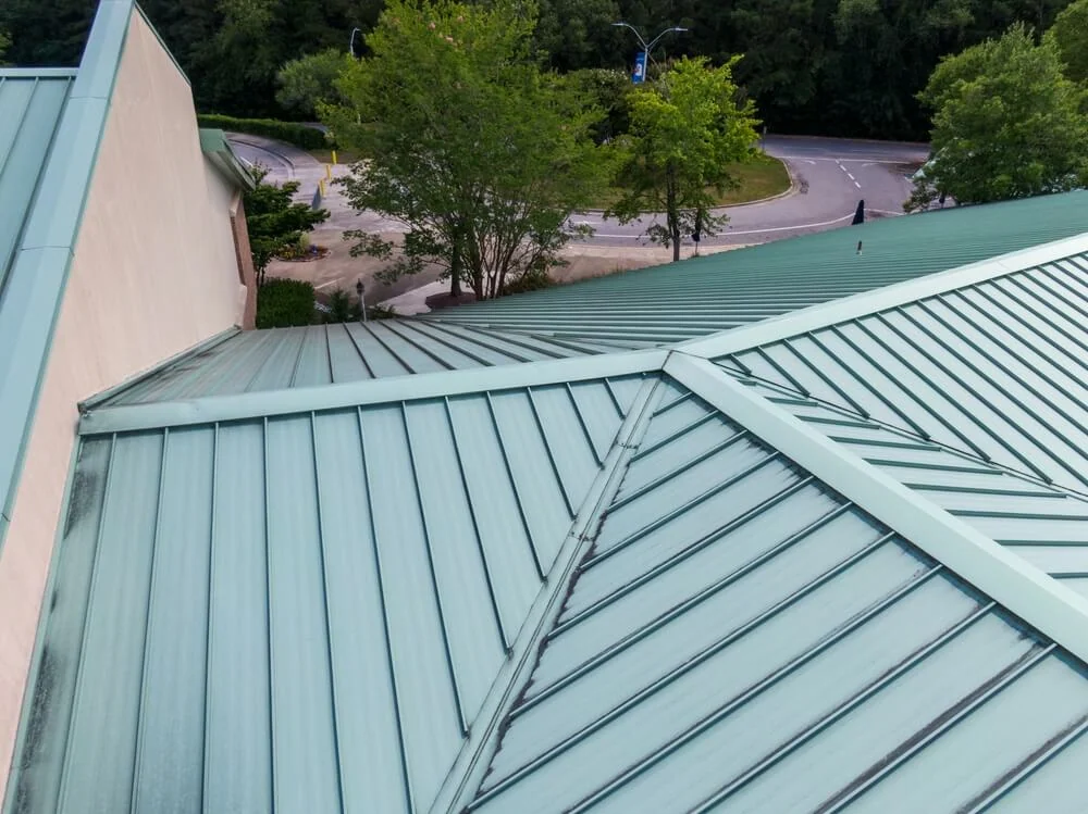 A geometric green metal roof made from sustainable commercial roofing materials, surrounded by trees and a curved road, showcases EPDM and TPO solutions.