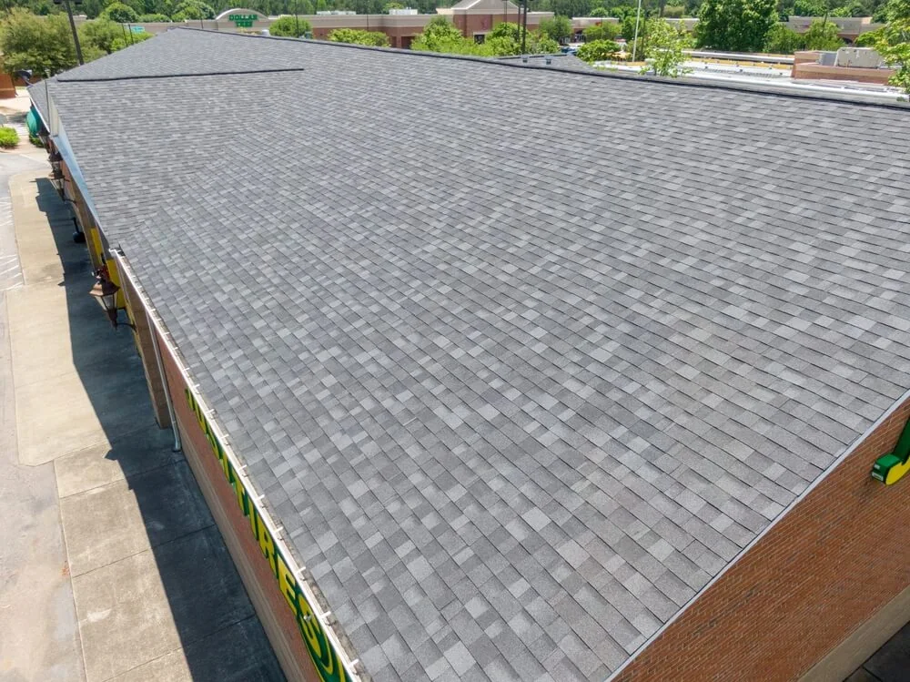 A long commercial building covered in gray asphalt architectural shingles.